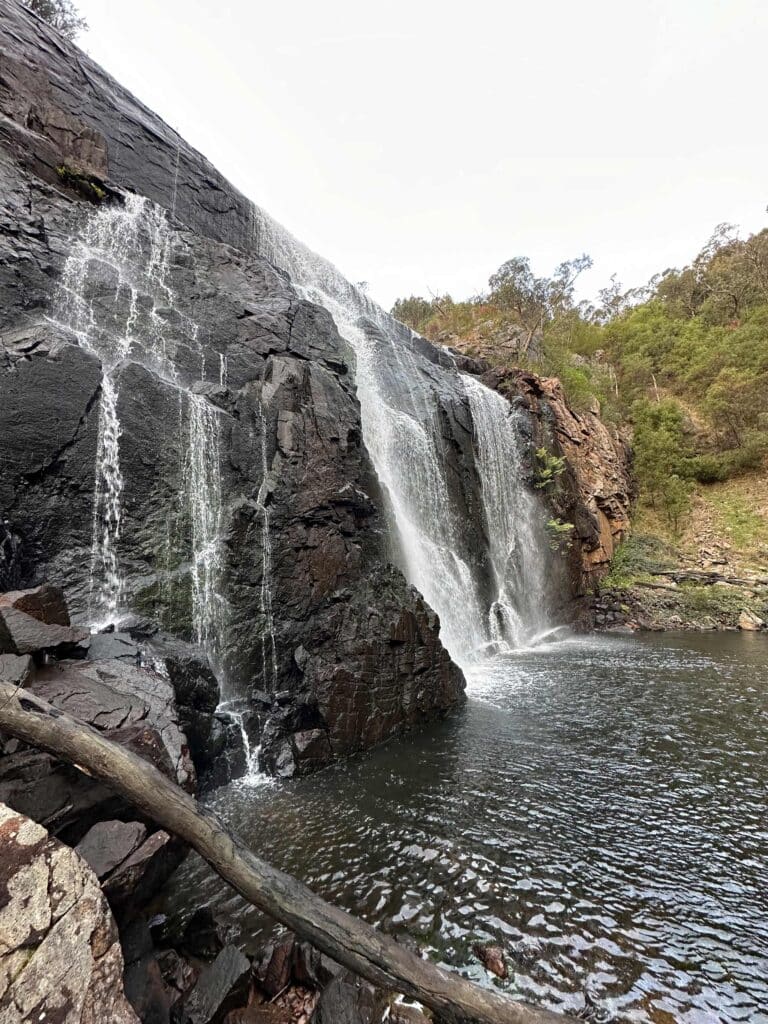 A beautiful waterfall cascading down a rocky cliff into a serene pool, surrounded by lush greenery and trees